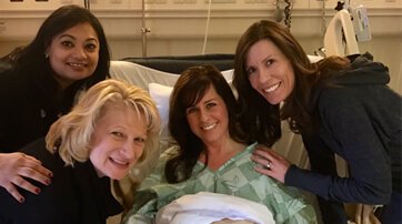 Three female colleagues surround Quest Diagnostics employee Kelley Bundick in her hospital bed as she recovers from kidney donor surgery.